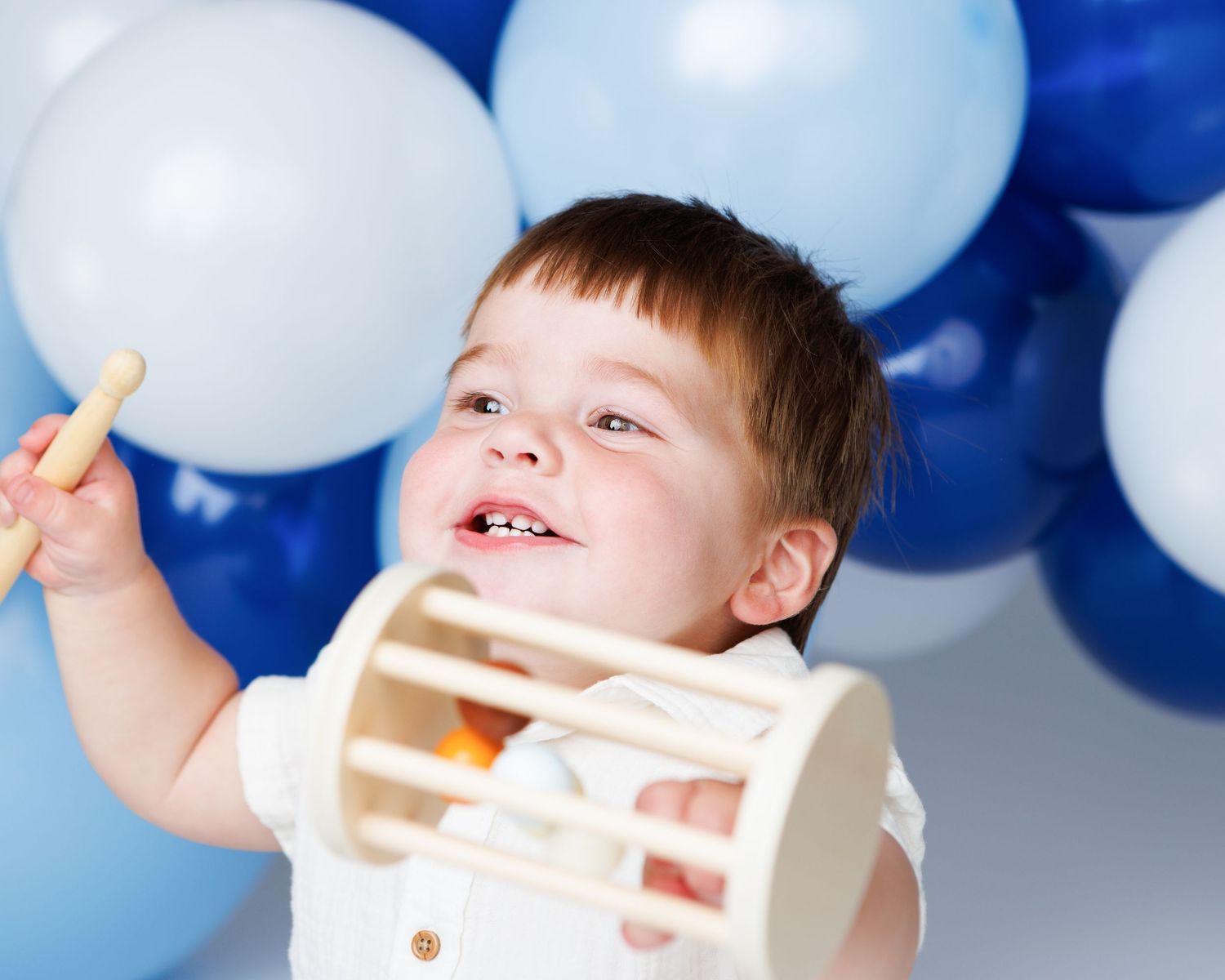 One-year-old boy playing in front of blue and white balloons during a Salem NH cake smash portrait session