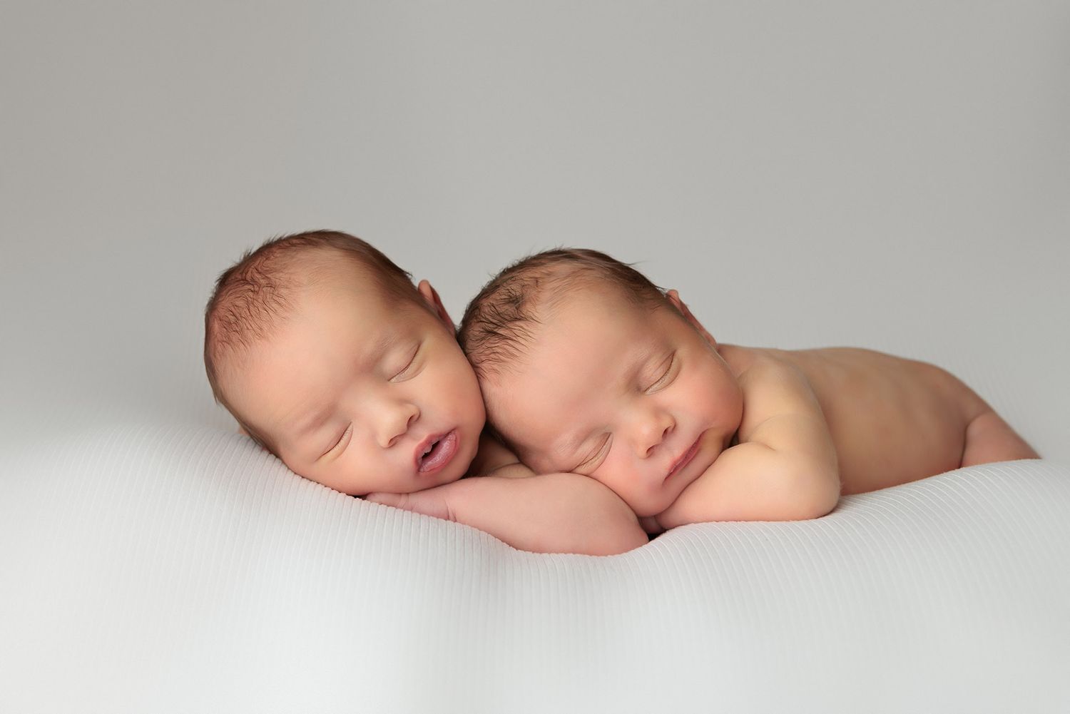 Two sleeping newborn twins lying side by side on a white blanket in a peaceful studio newborn photography session.