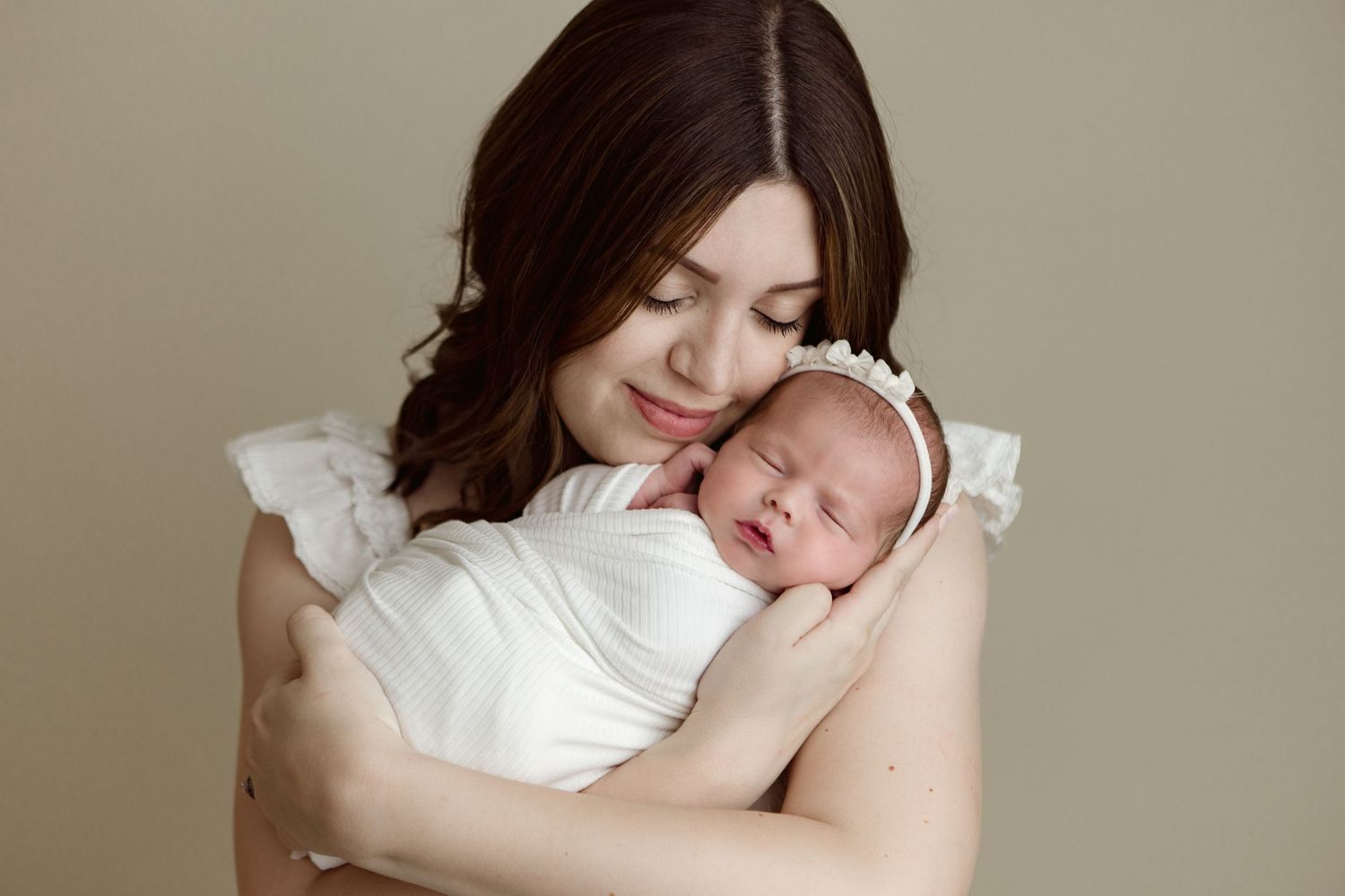 A tender moment captured as a mother in white holds her sleeping newborn baby against her shoulder.