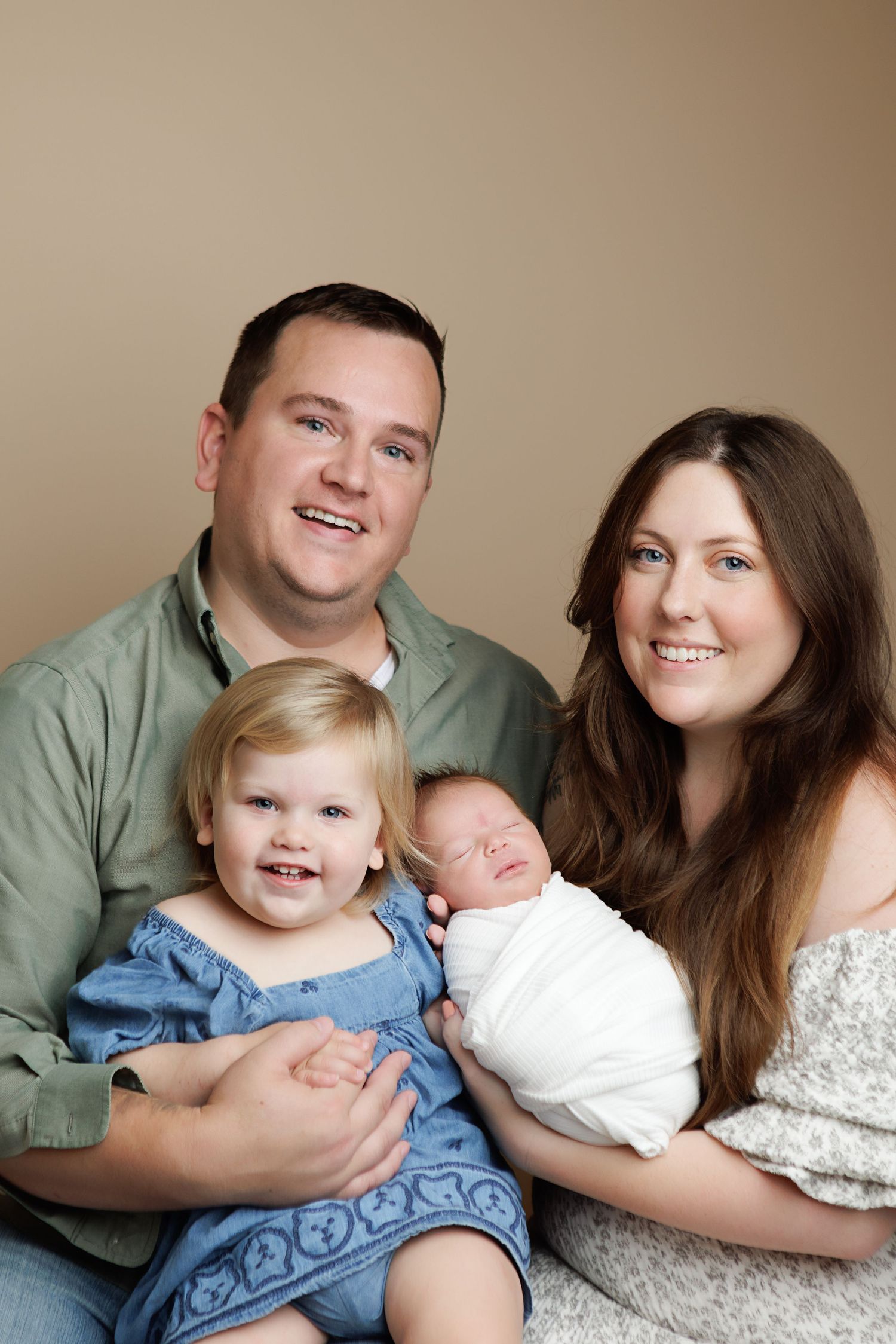 A family lying together on a beige backdrop in a series of connected portrait photos showing tender moments with a newborn.