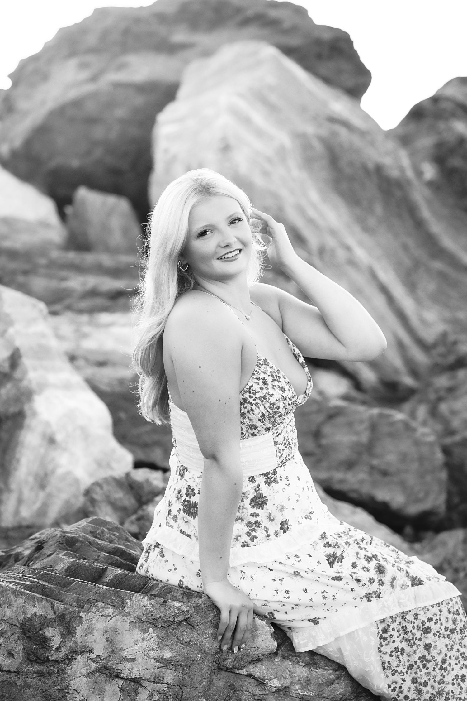 Black and white portrait of a High School Senior in a floral dress posing on rocky terrain during an outdoor photoshoot.