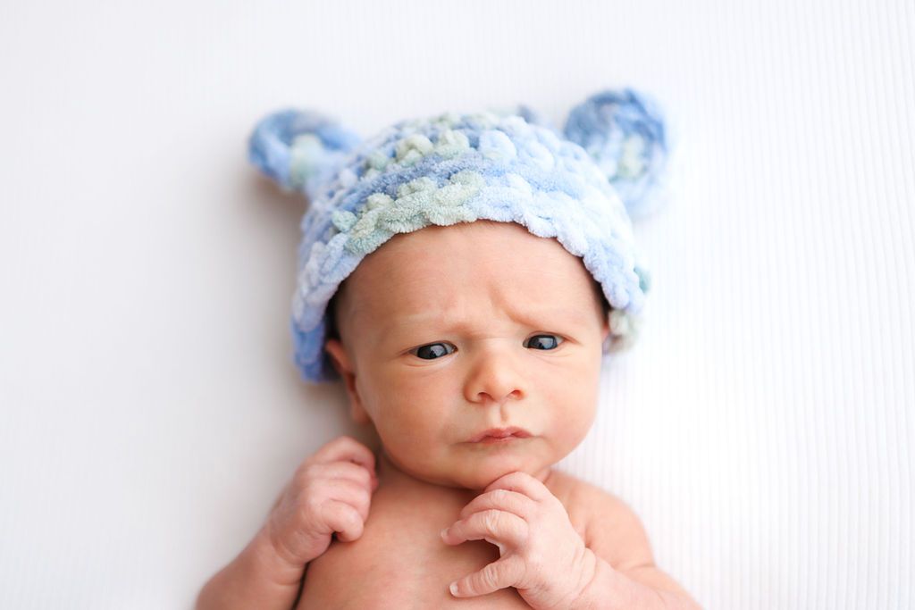Adorable newborn baby wearing a blue knitted bear hat lying on white background.