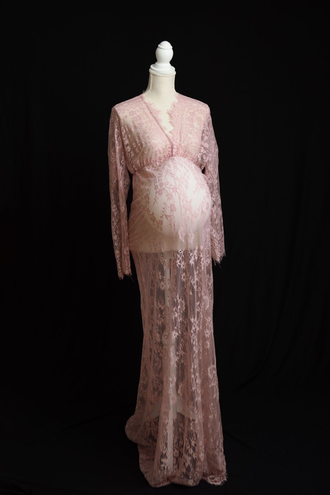 Vintage-style pink lace dress with long sleeves displayed on a white mannequin against a dark background.