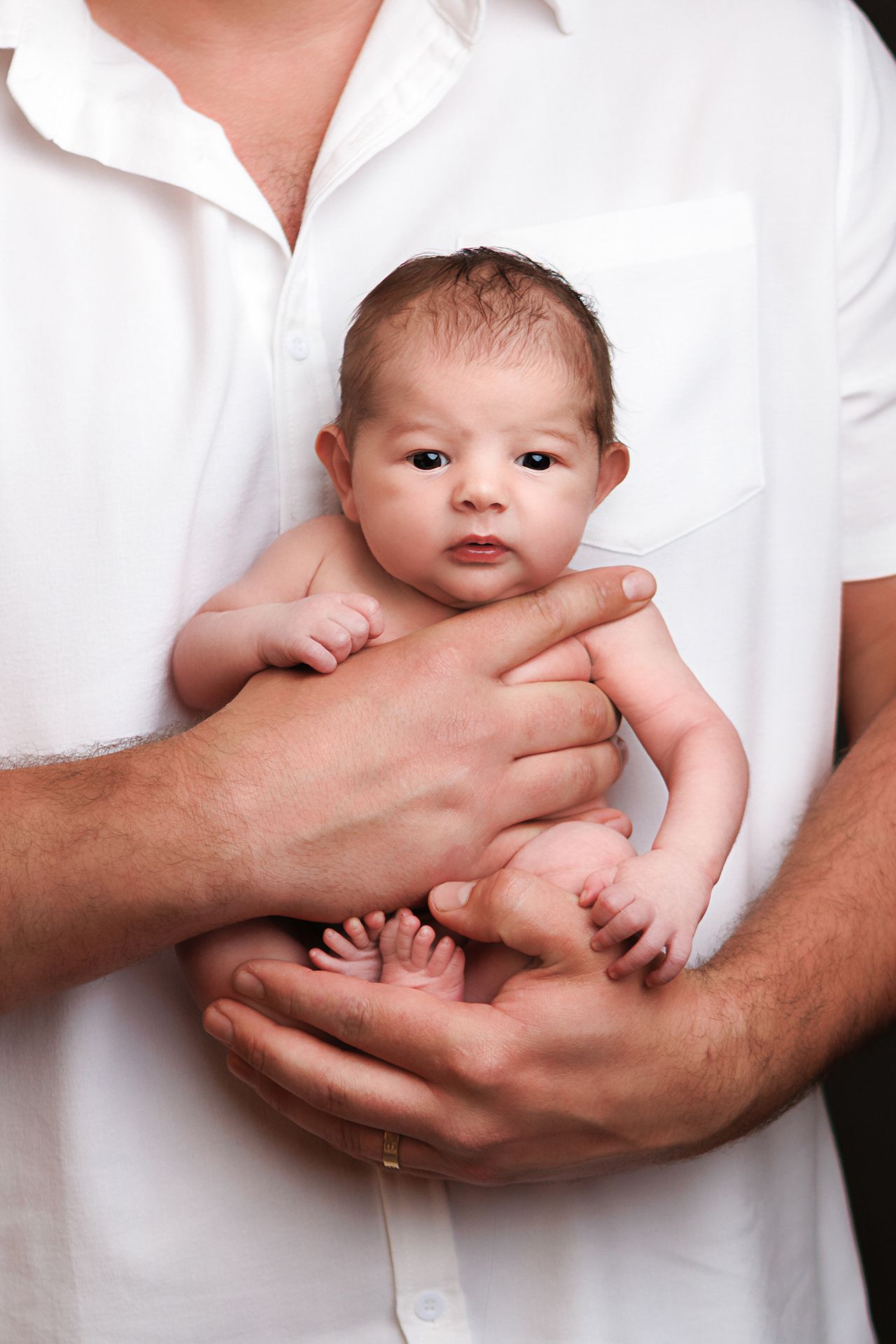 Father in white shirt cradling newborn baby in his hands, close-up portrait of infant and parent.