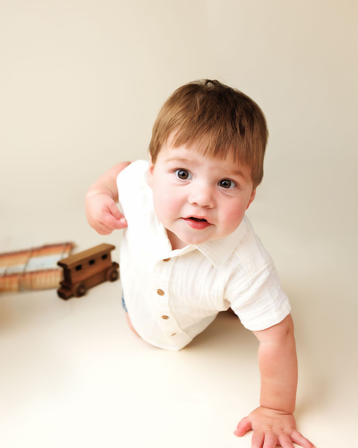 Crawling baby boy with a wooden train during the clean portrait portion of a cake smash session