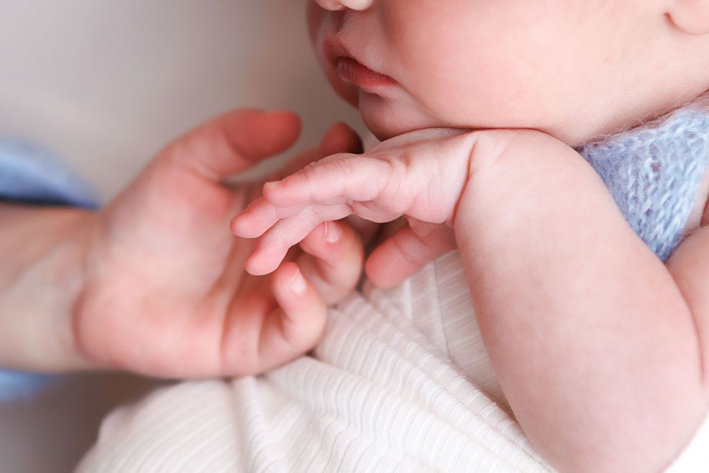 Close-up of a newborn baby grasping an adult's finger, wearing a soft blue outfit.