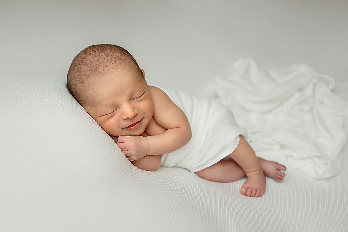 Peaceful newborn baby sleeping on soft white blankets in natural light during professional photography session.