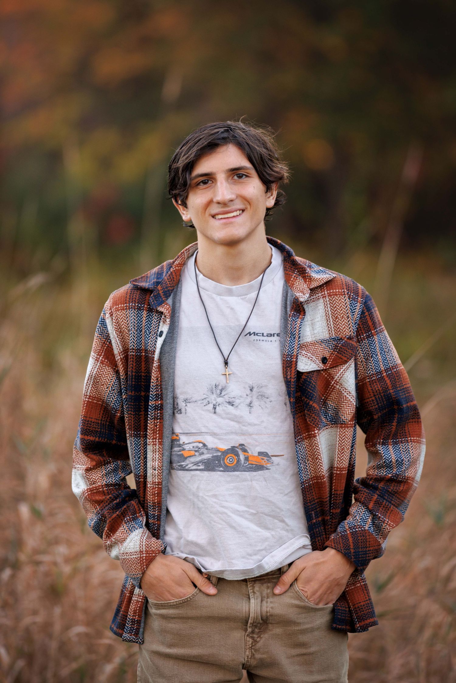 High School Senior wearing a plaid flannel shirt and white t-shirt poses in an outdoor field during autumn.