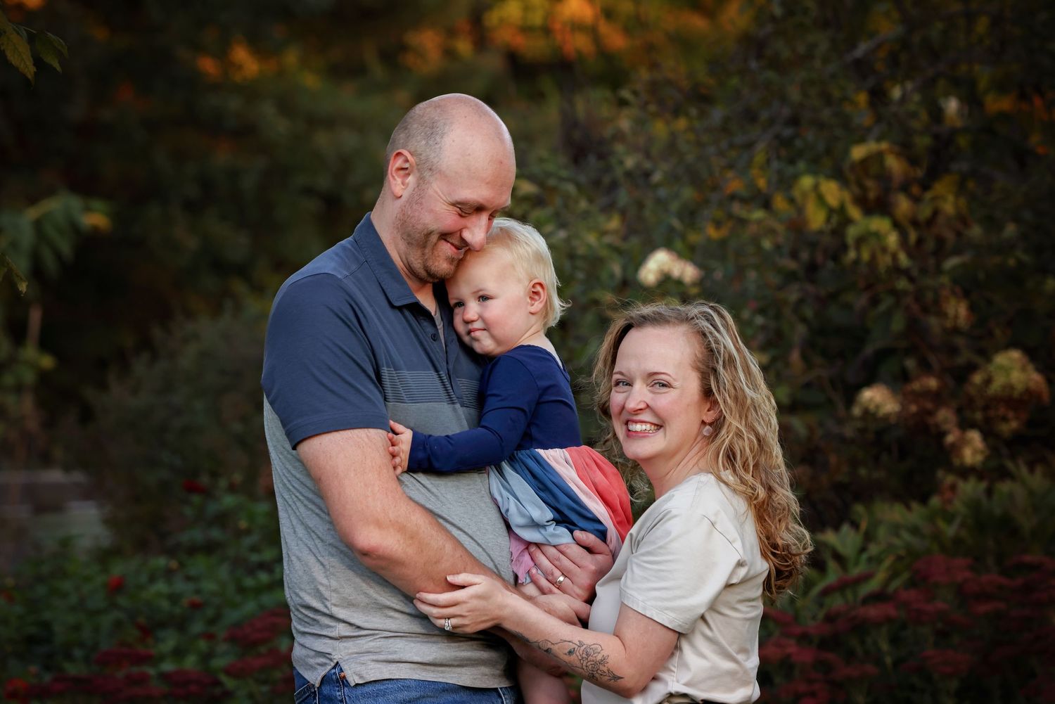 A loving family moment outdoors during autumn with fall foliage in the background.