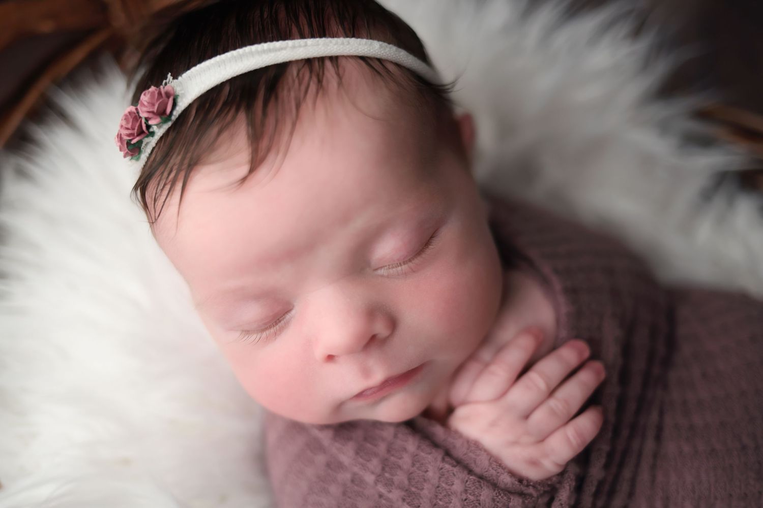 A sleeping newborn baby swaddled in soft gray blankets rests peacefully on white fur bedding.