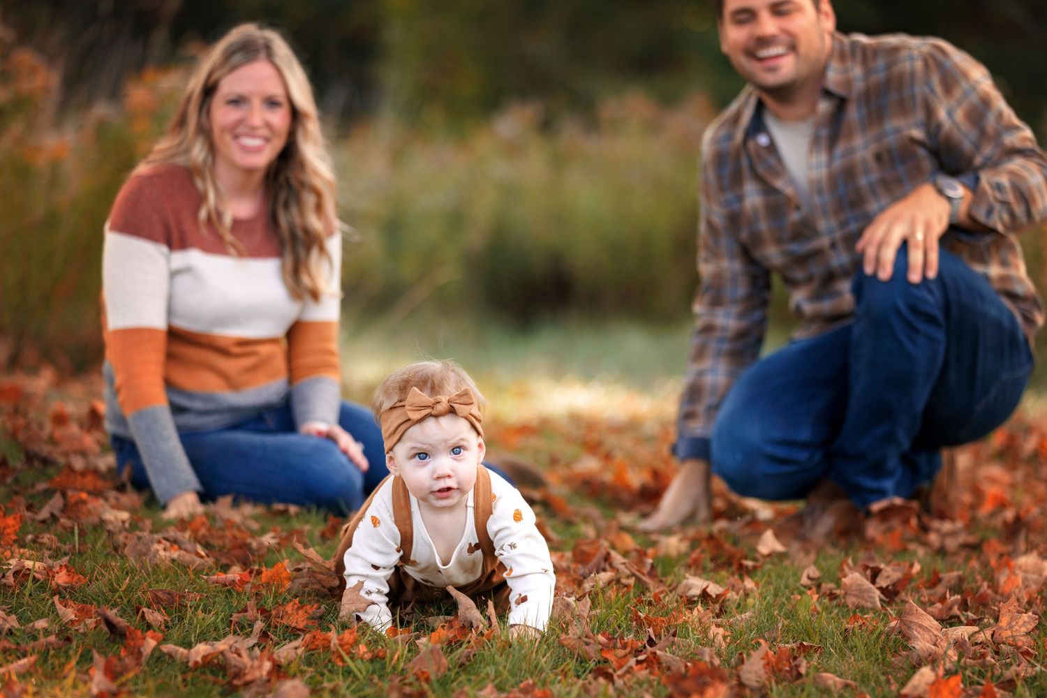 A family sits together on fallen autumn leaves during an outdoor photo session in a park setting.