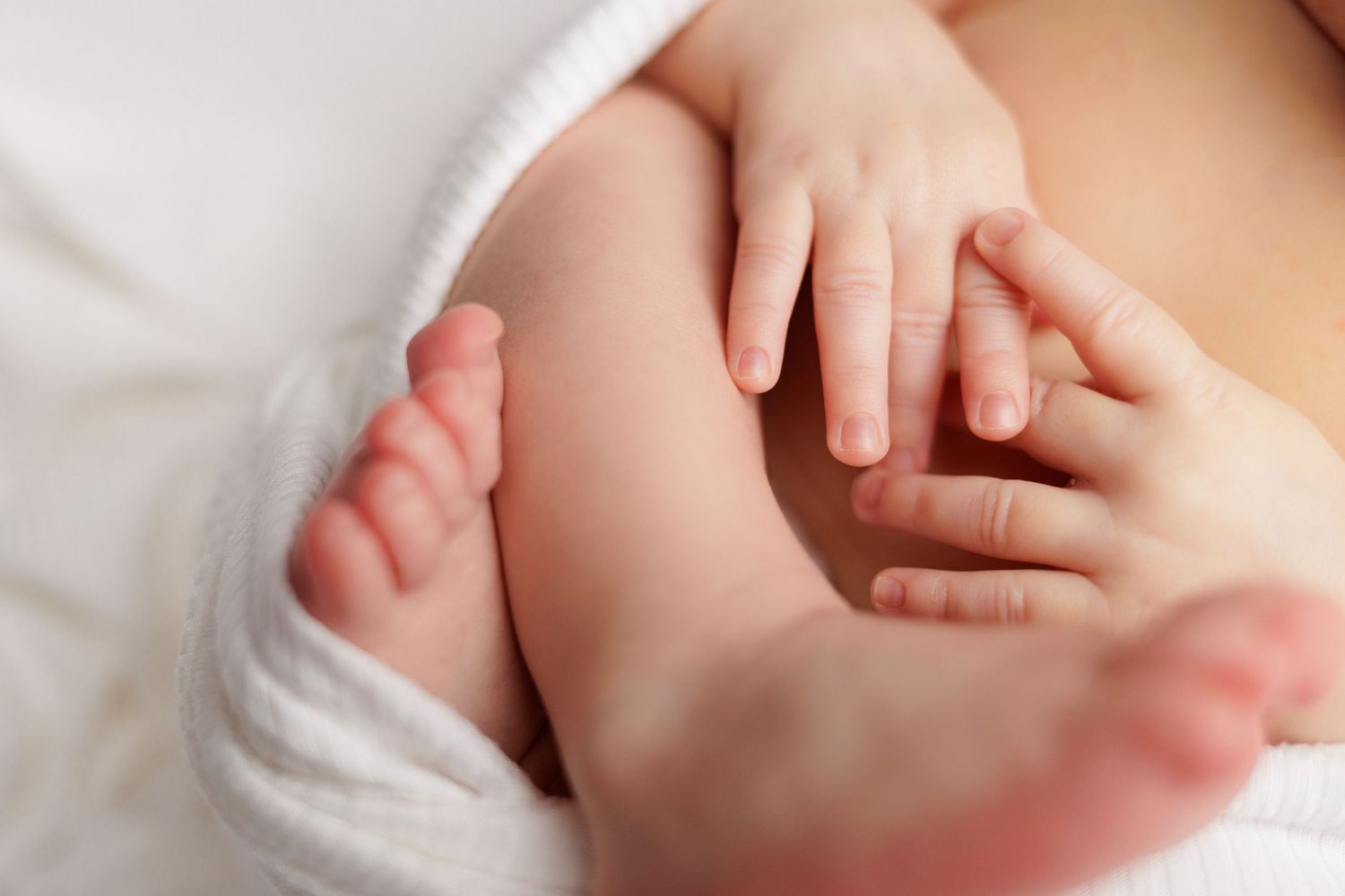 A close-up view of tiny newborn baby feet wrapped in soft white blankets.