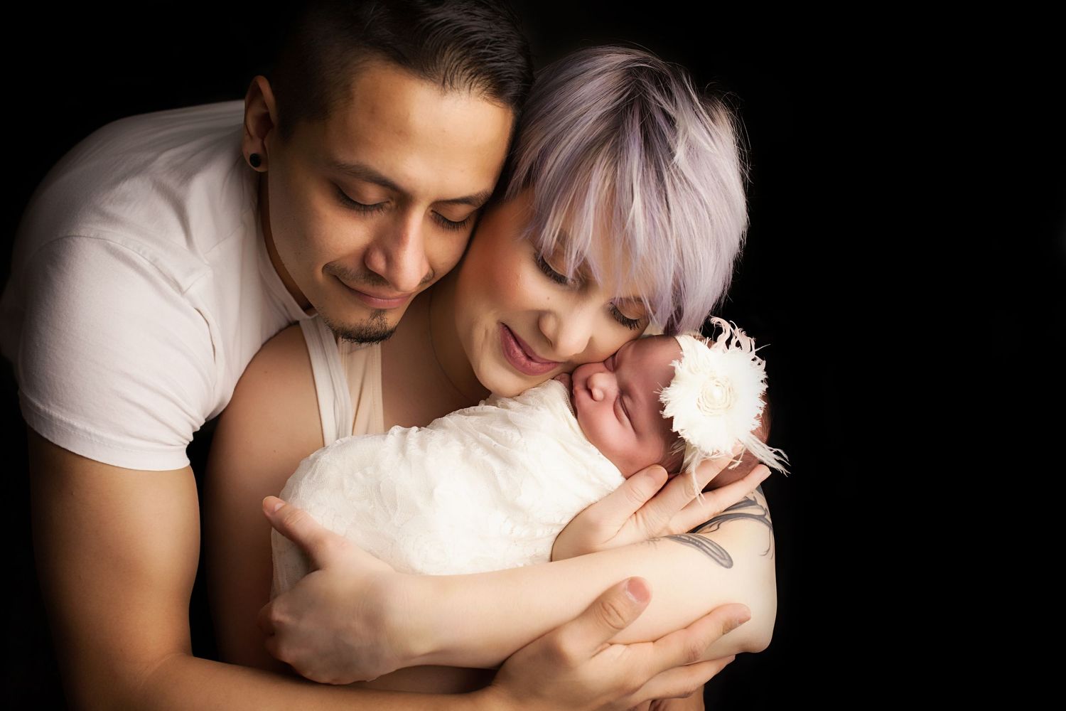A tender embrace between Mother, Father and newborn infant wearing white and pink, captured in an intimate black and white series.