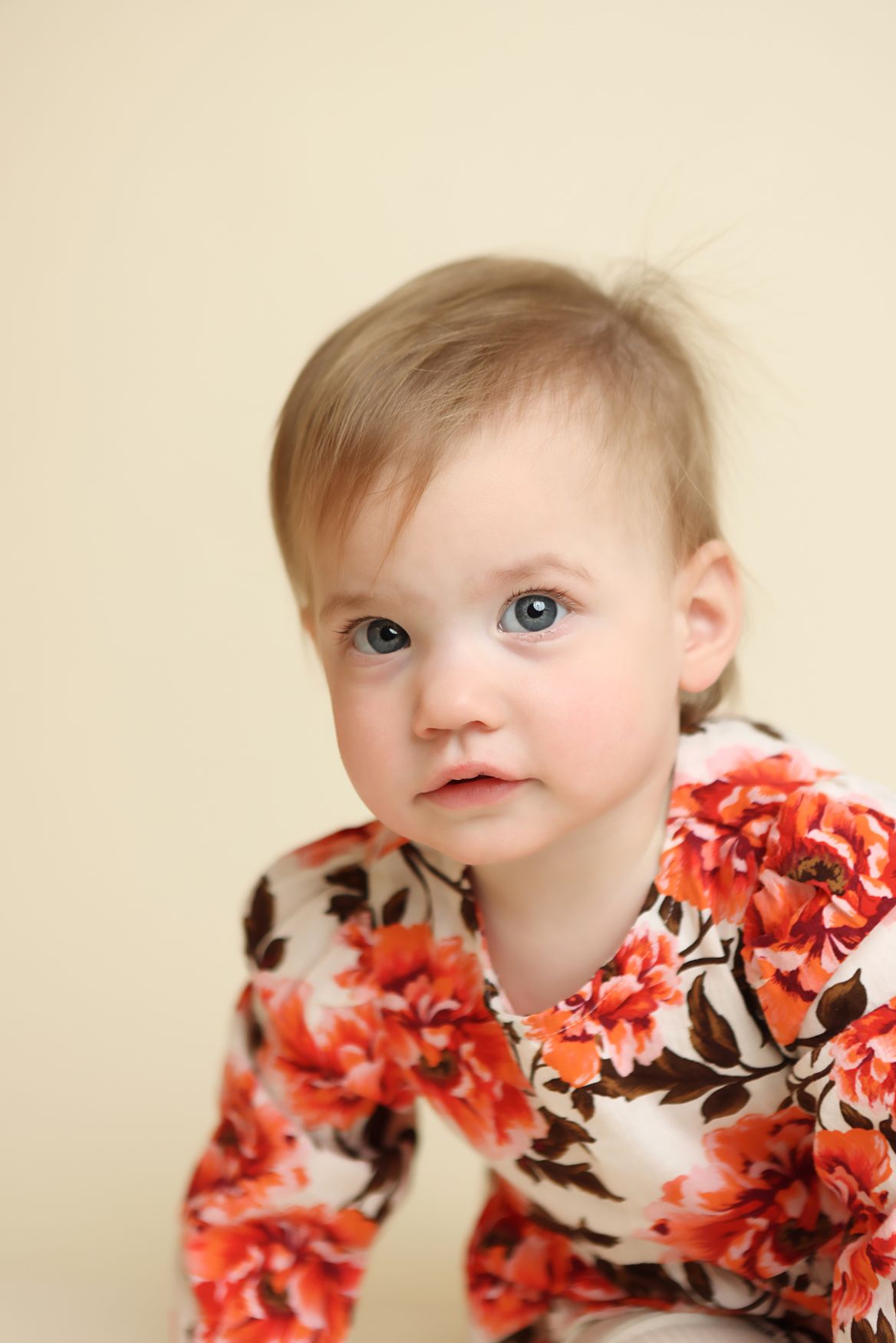 A series of close-up portraits showing a baby in a floral print outfit against a cream background.