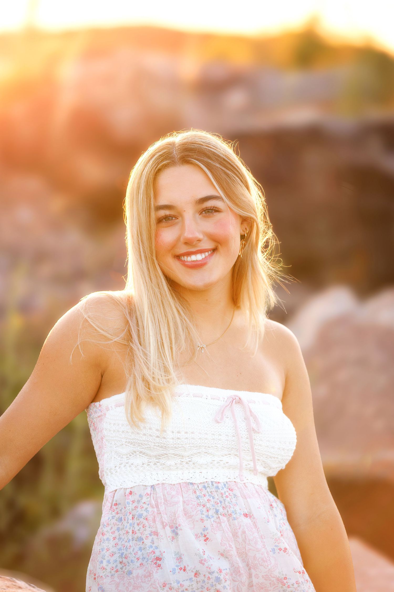 A person in a white floral sundress poses outdoors during golden hour sunset lighting.