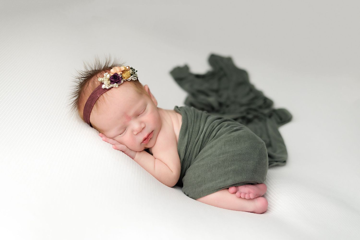 A sleeping newborn baby in green clothing lies on white bedding in a series of connected artistic photos.