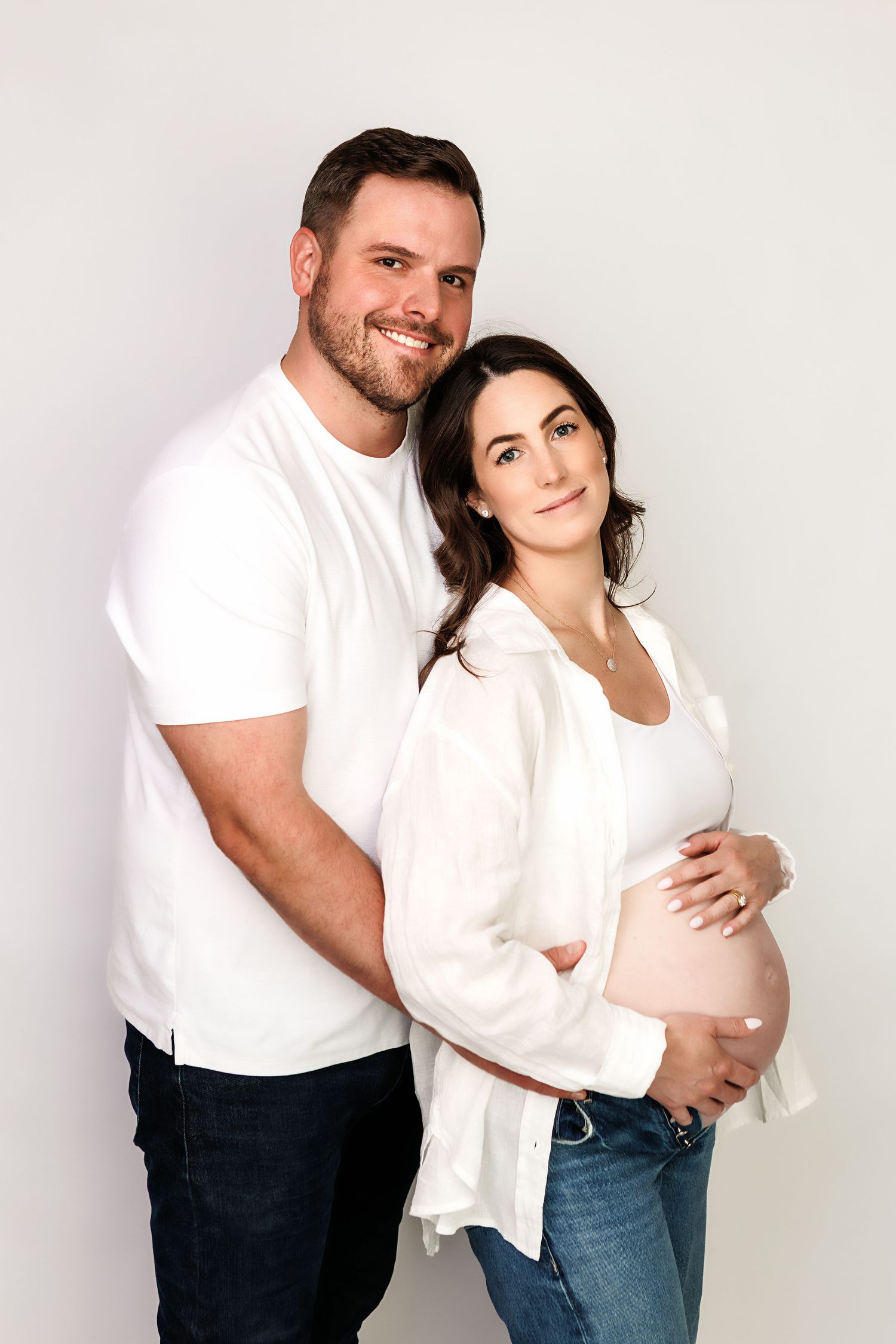 Happy couple posing for maternity photo, man in white t-shirt embracing pregnant woman in white shirt and jeans.