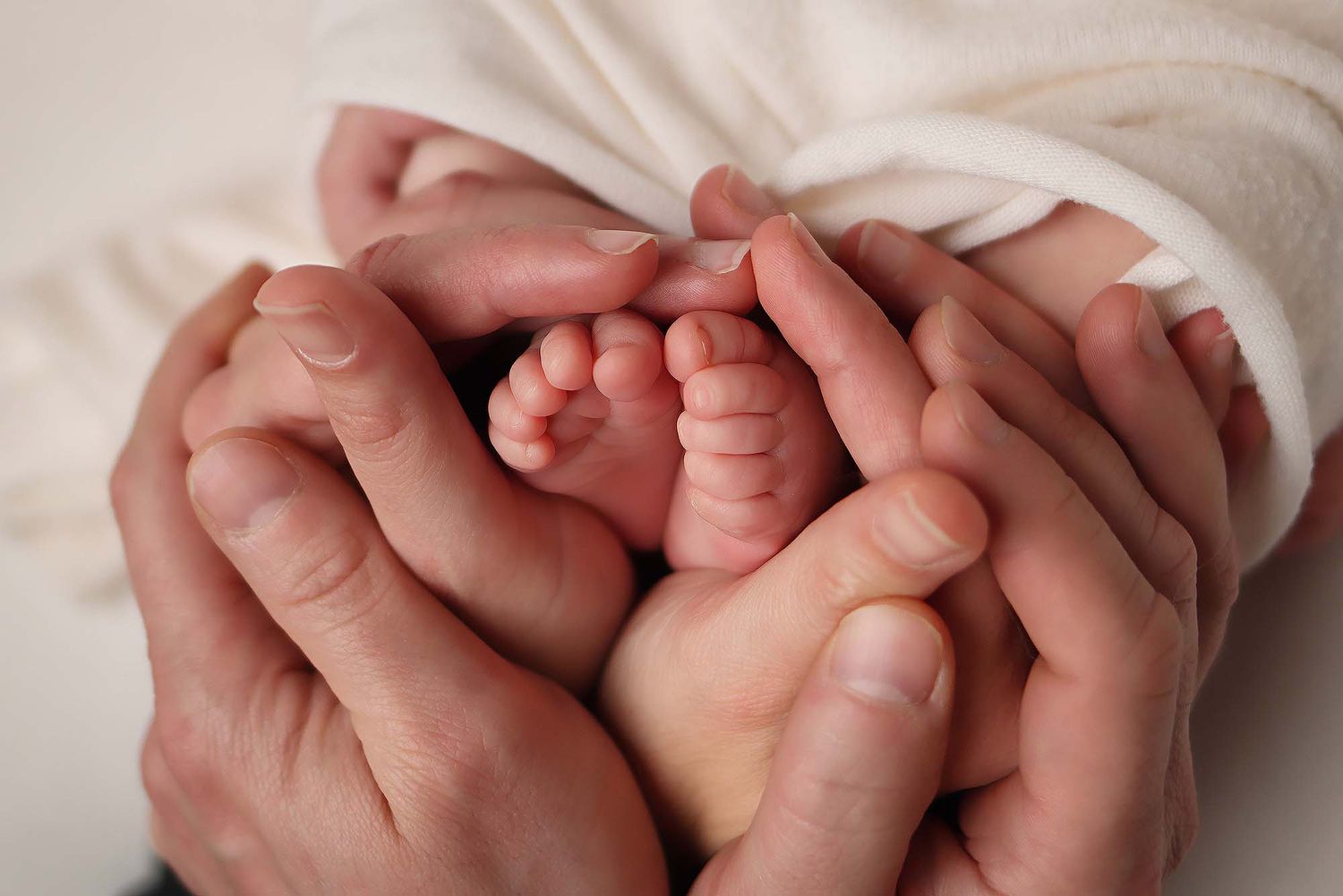 A close-up series of tiny newborn baby feet being gently held by adult hands against a white background.