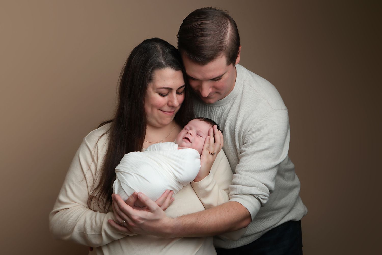 A series of intimate family photos showing tender moments with a newborn baby in a neutral brown studio setting.