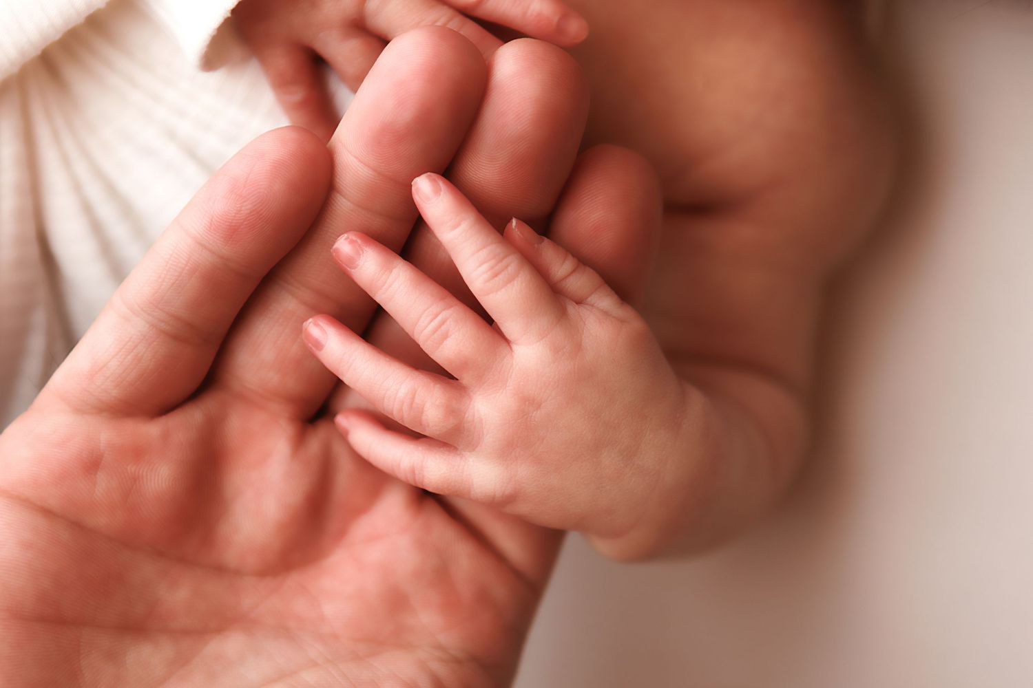A close-up view of baby hands grasping and reaching against a soft white background.