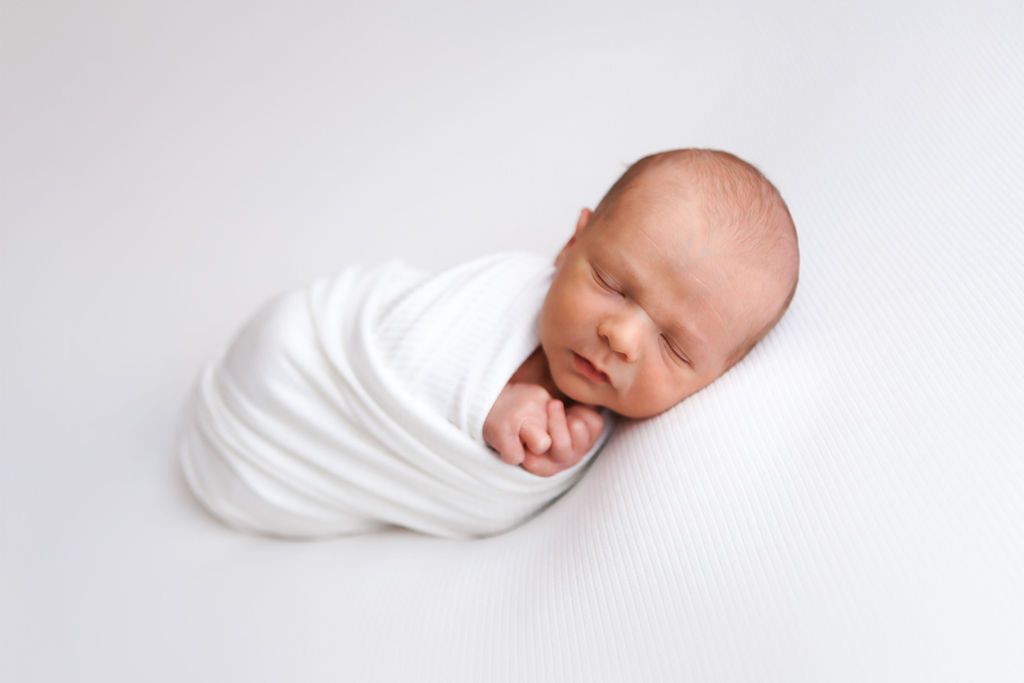 Peaceful newborn baby swaddled in white wrap sleeping on white background in professional studio photo.