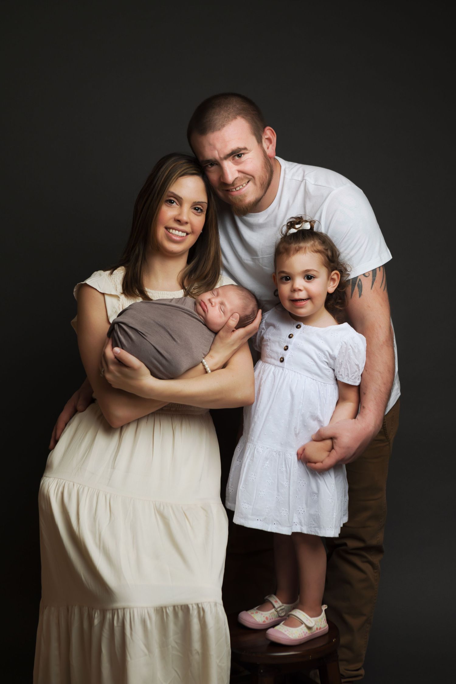 Studio portrait of a family of four against a dark background, dressed in casual attire.