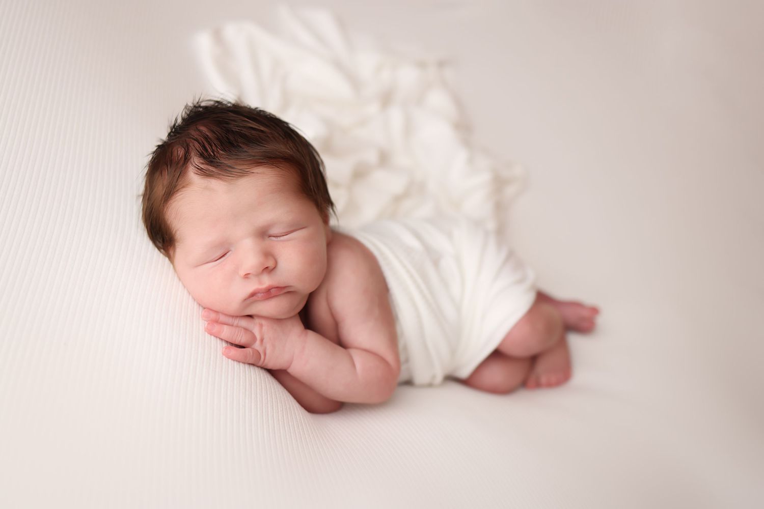 Sleeping newborn baby wrapped in soft white blanket on neutral background.