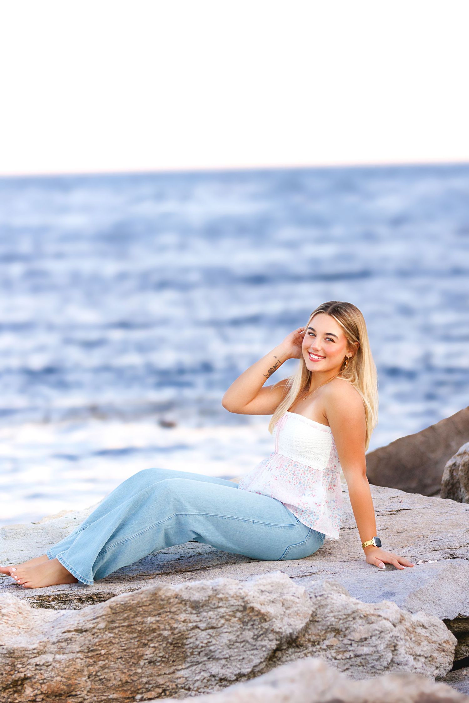 A mermaid-inspired photoshoot on rocky coastal terrain with flowing blue fabric and white top against ocean waves.