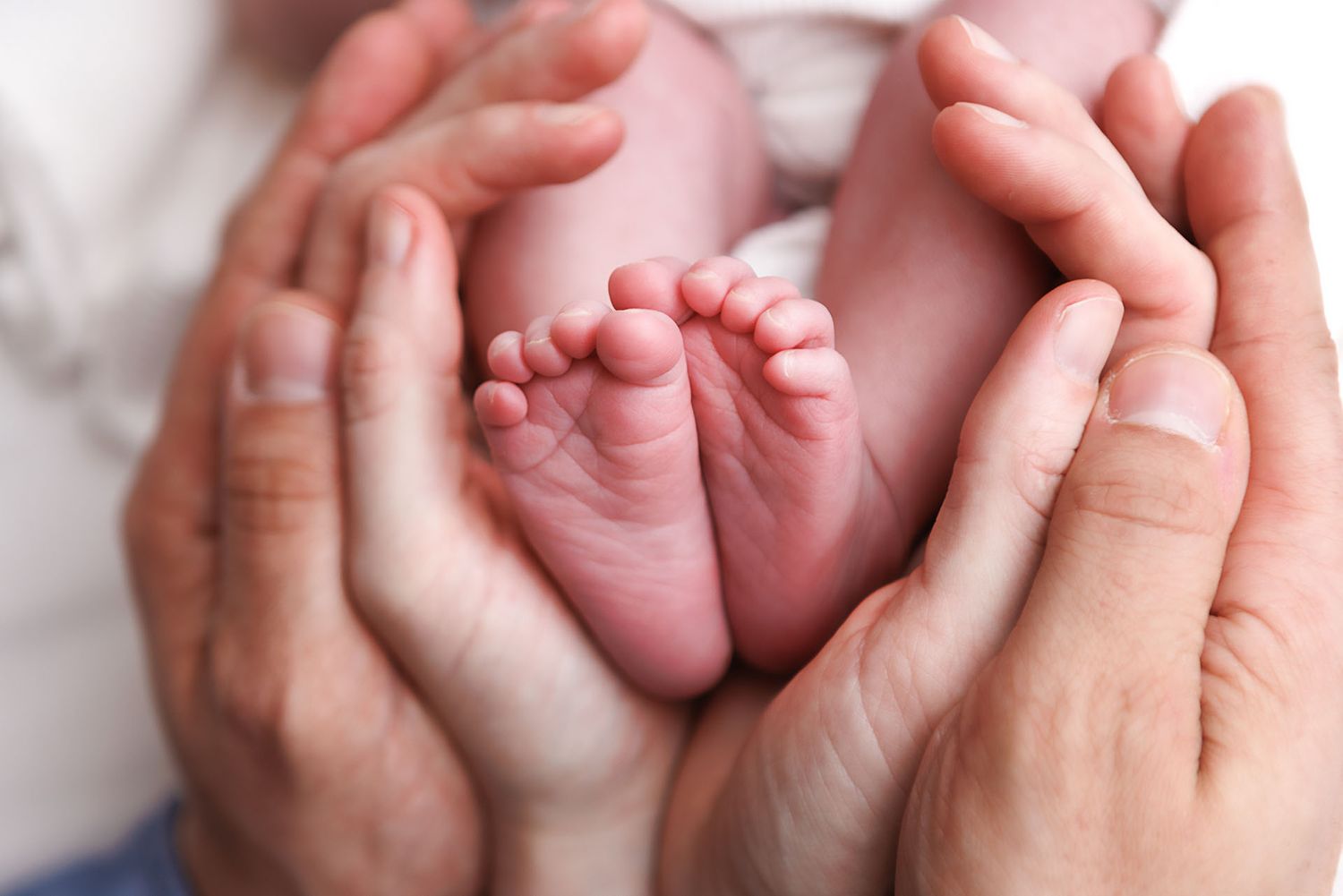 Adult hands cradling tiny newborn baby feet in a heart shape, symbolizing parental love and new life.