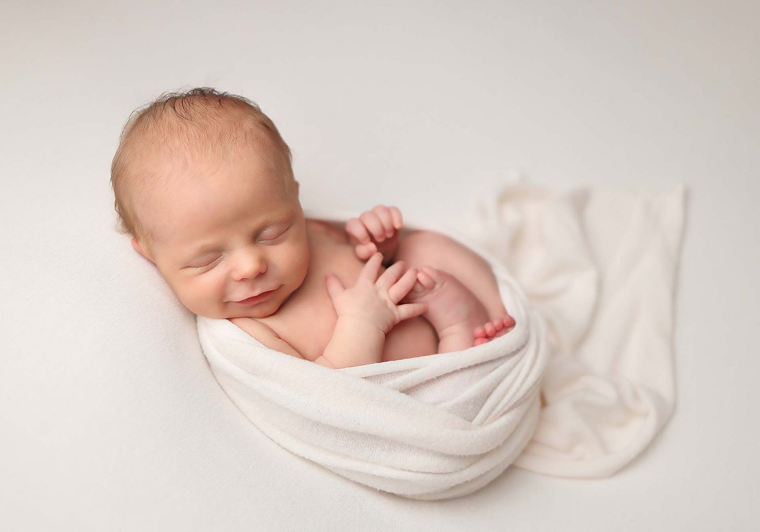 Newborn baby wrapped in soft white fabric sleeps peacefully in artistic black and white photography.