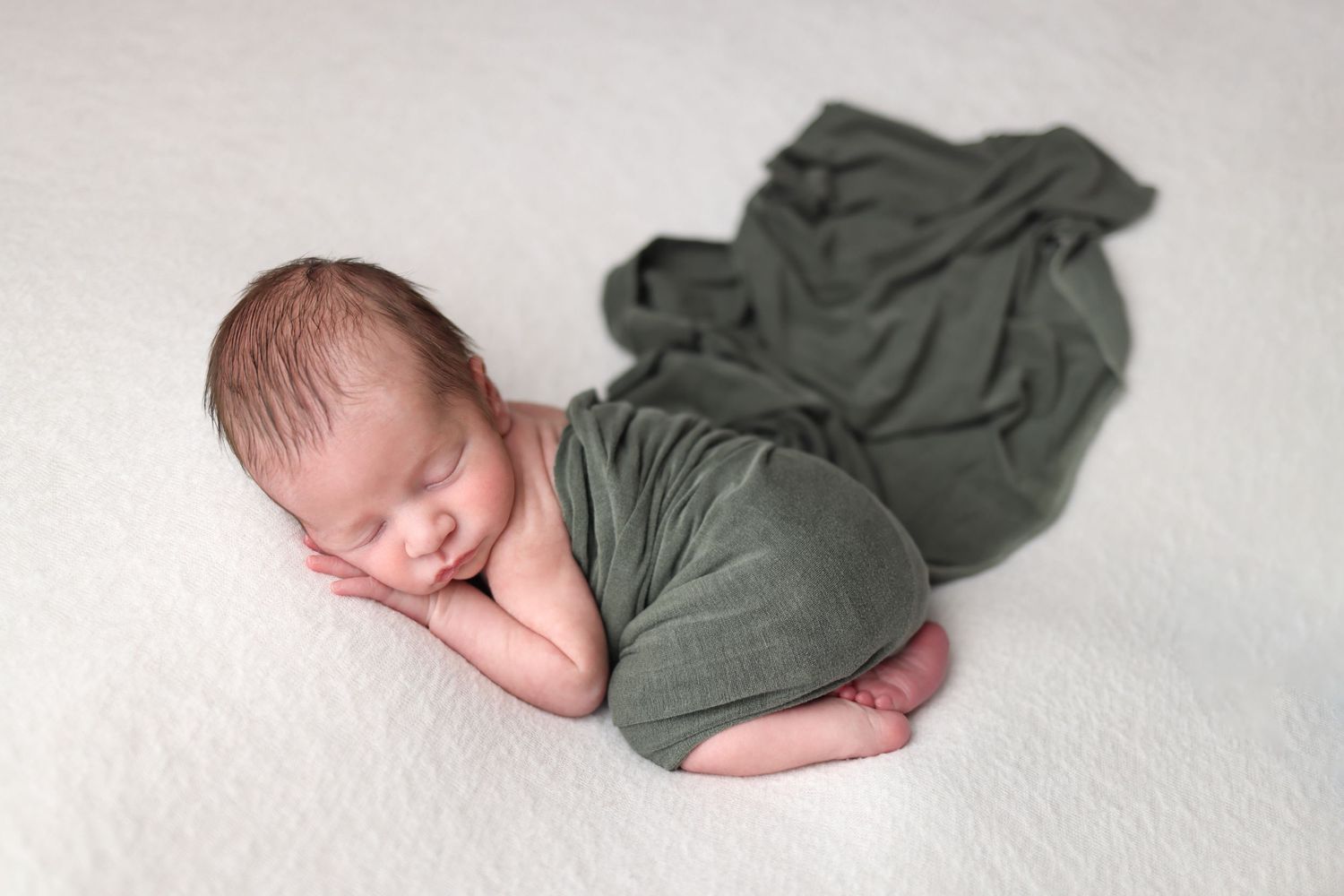 A series of four connected photos showing a sleeping newborn baby wrapped in an olive green blanket.