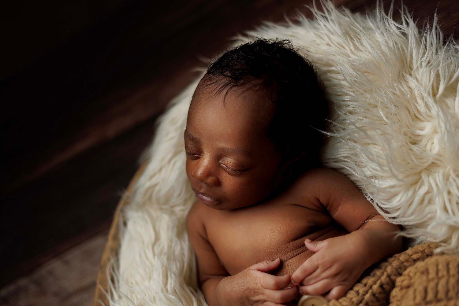 Peaceful newborn sleeping on soft white fur blanket in dark moody lighting.