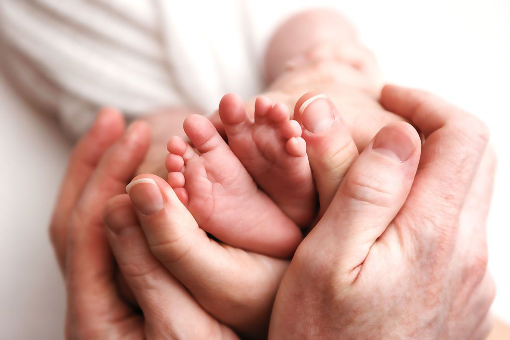 Adult hands lovingly cradle tiny newborn baby feet in a close-up photography portrait.