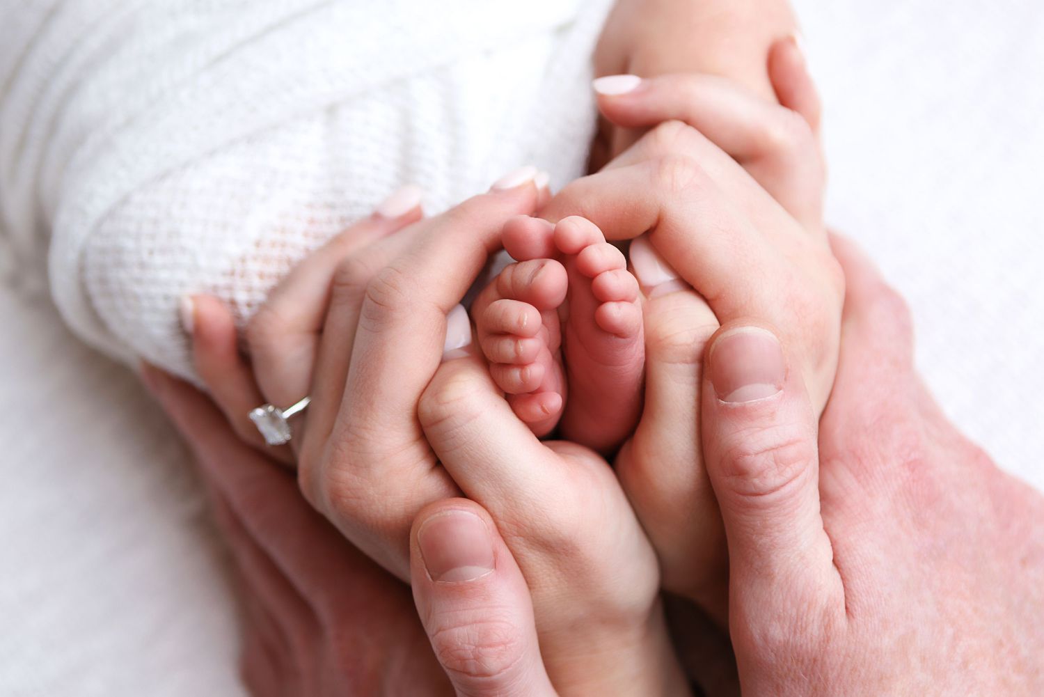 Close-up view of a newborn baby's tiny hand grasping an adult's finger in a tender moment.