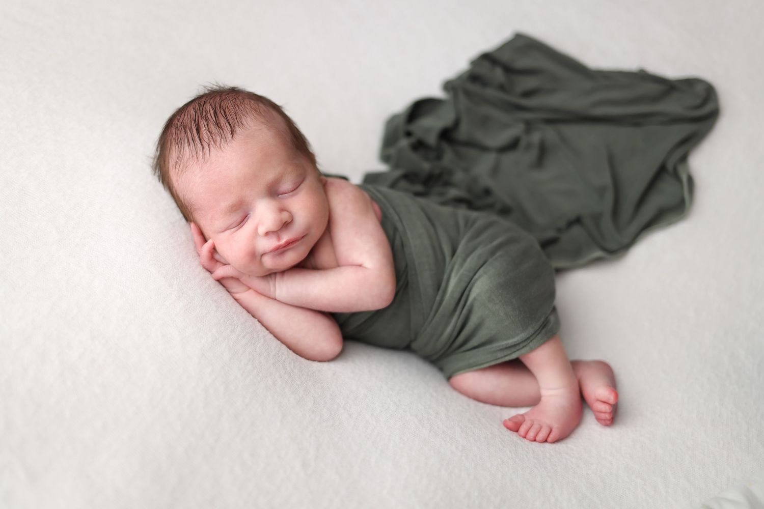 Newborn baby sleeping peacefully in olive green wrap during professional photo session.