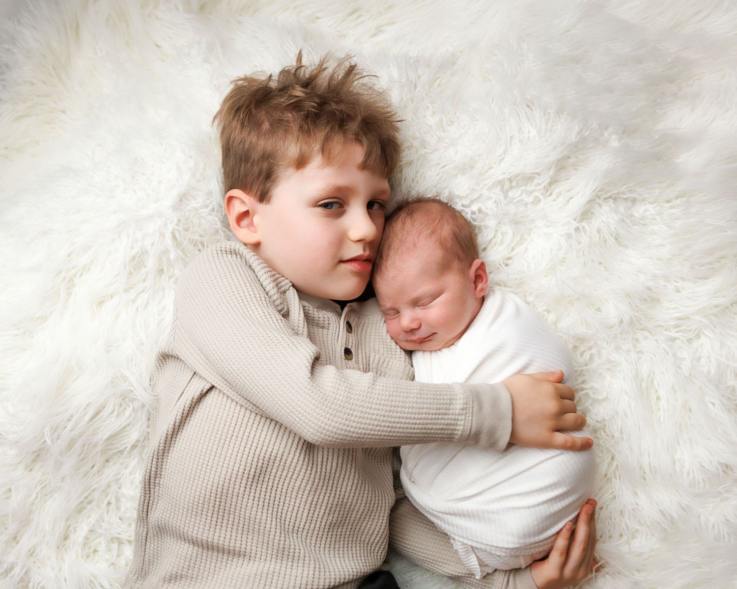 Older brother holding his newborn sibling during a newborn photography session in Salem New Hampshire