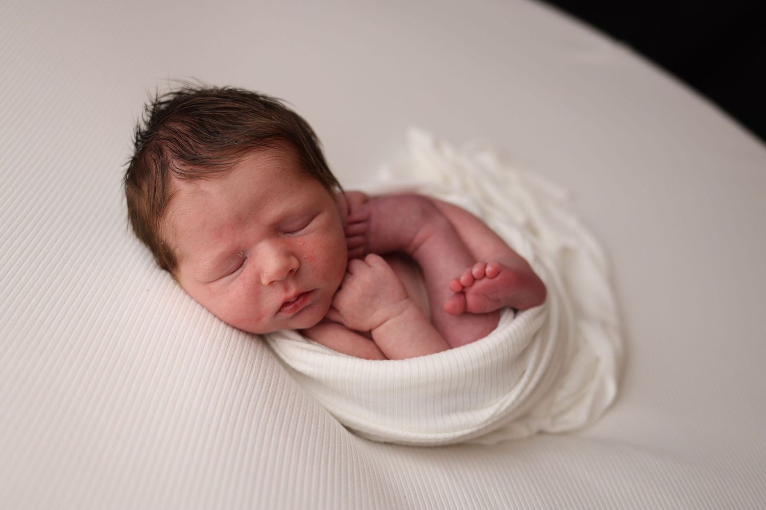 A series of four connected images showing a sleeping newborn baby wrapped in white swaddling cloth.