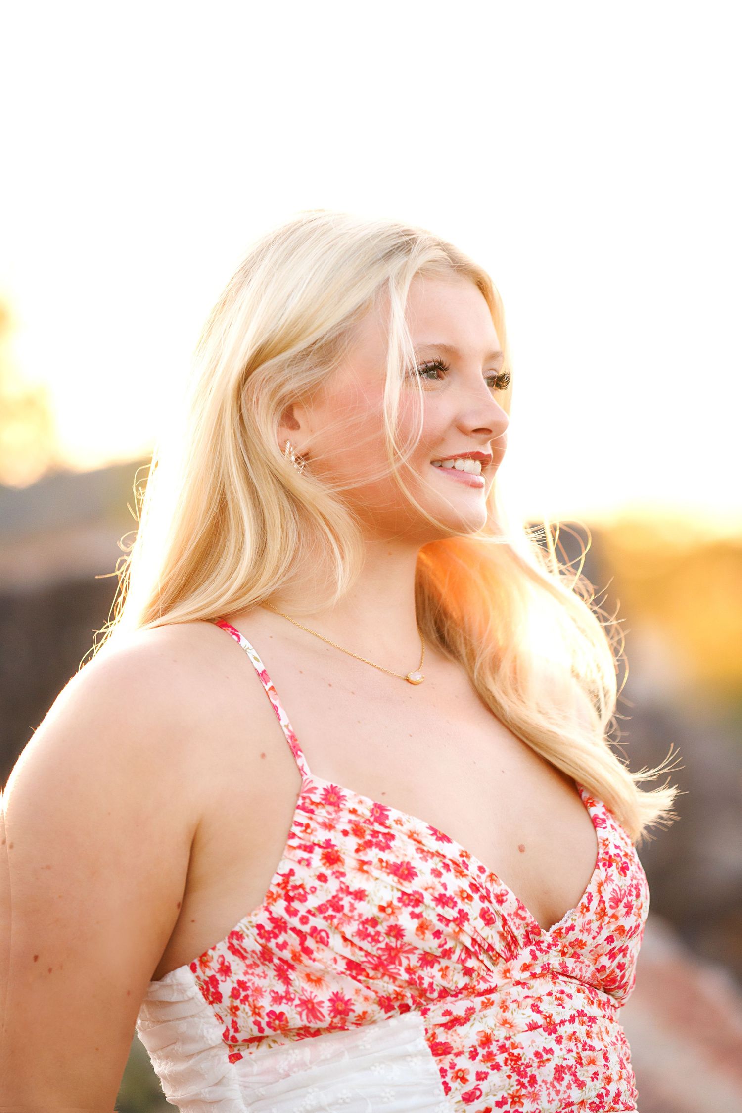 A person in a red and white floral dress poses outdoors during golden hour sunset.