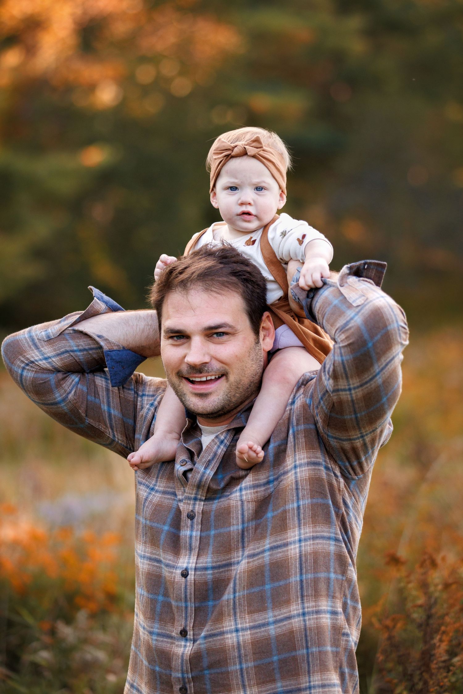 A heartwarming autumn moment captured as a baby rides on shoulders against blurred fall colors.