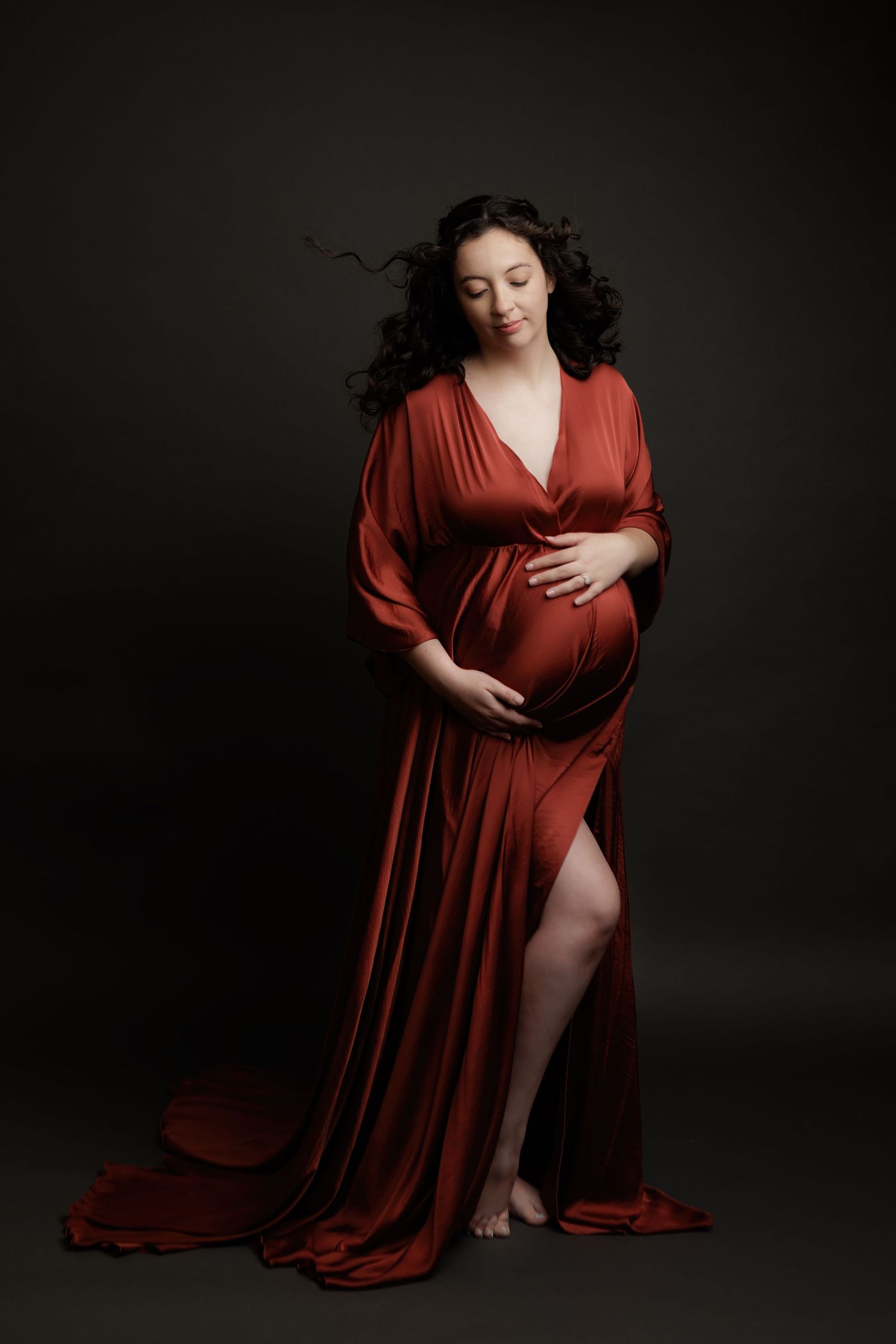A woman in a flowing burgundy dress poses gracefully against a dark background in a series of artistic portraits.