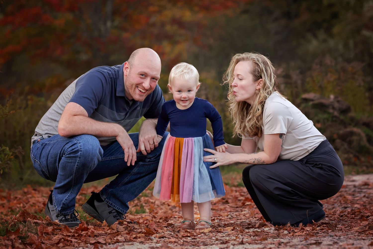 A family sits together on autumn leaves in a series of candid outdoor portraits during fall.