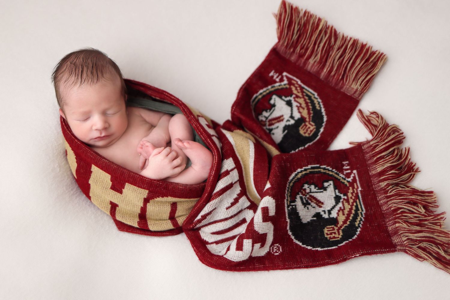 A sleeping newborn baby lies peacefully in a Florida State University football scarf.