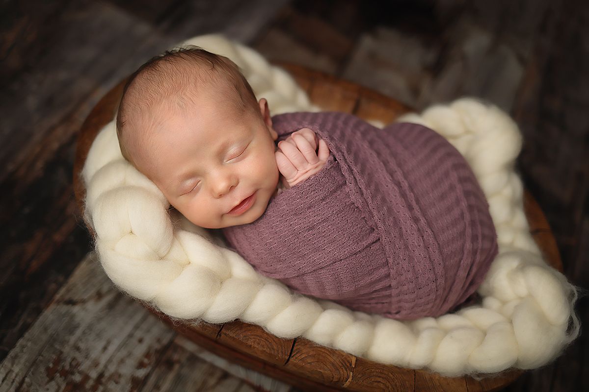 Newborn baby sleeping peacefully on soft white fur blanket in professional photography studio setting.