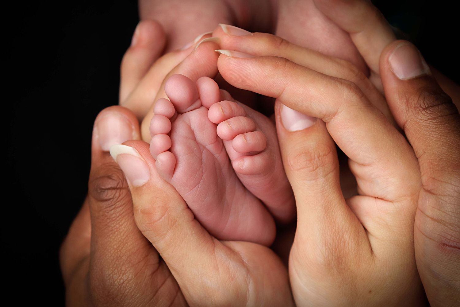 Close-up view of adult hands holding tiny newborn baby feet with gentle care.