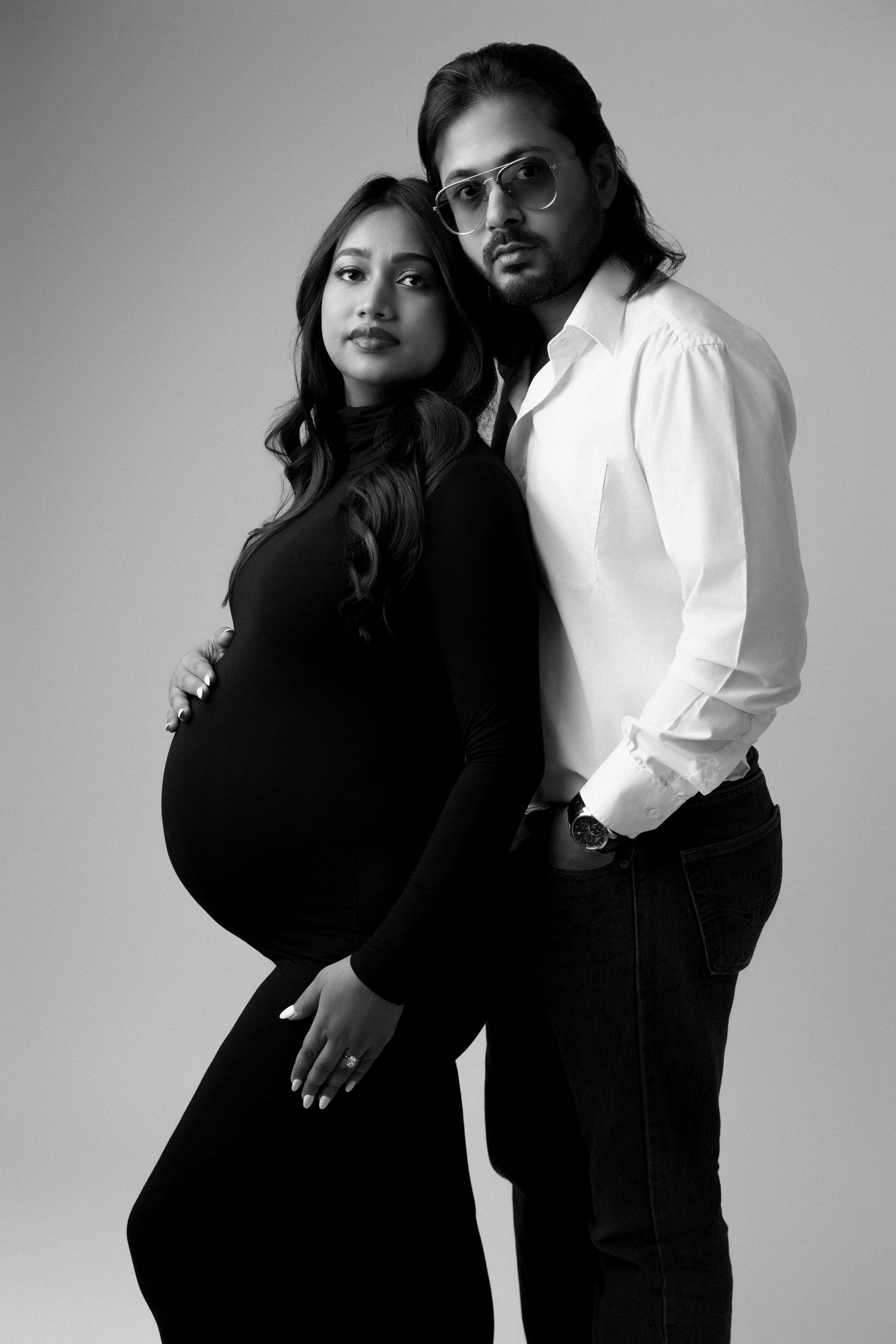 Black and white studio maternity portrait of couple in contrasting outfits.