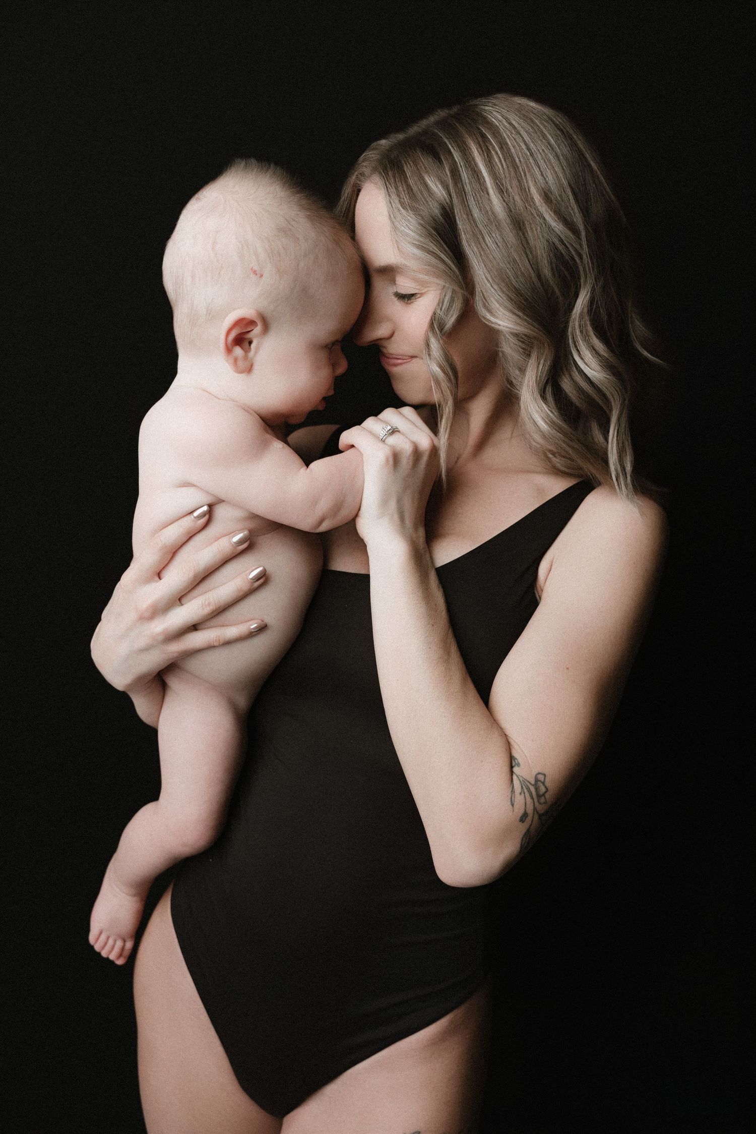 A tender black and white photo series showing intimate moments between parent and infant against a dark background.