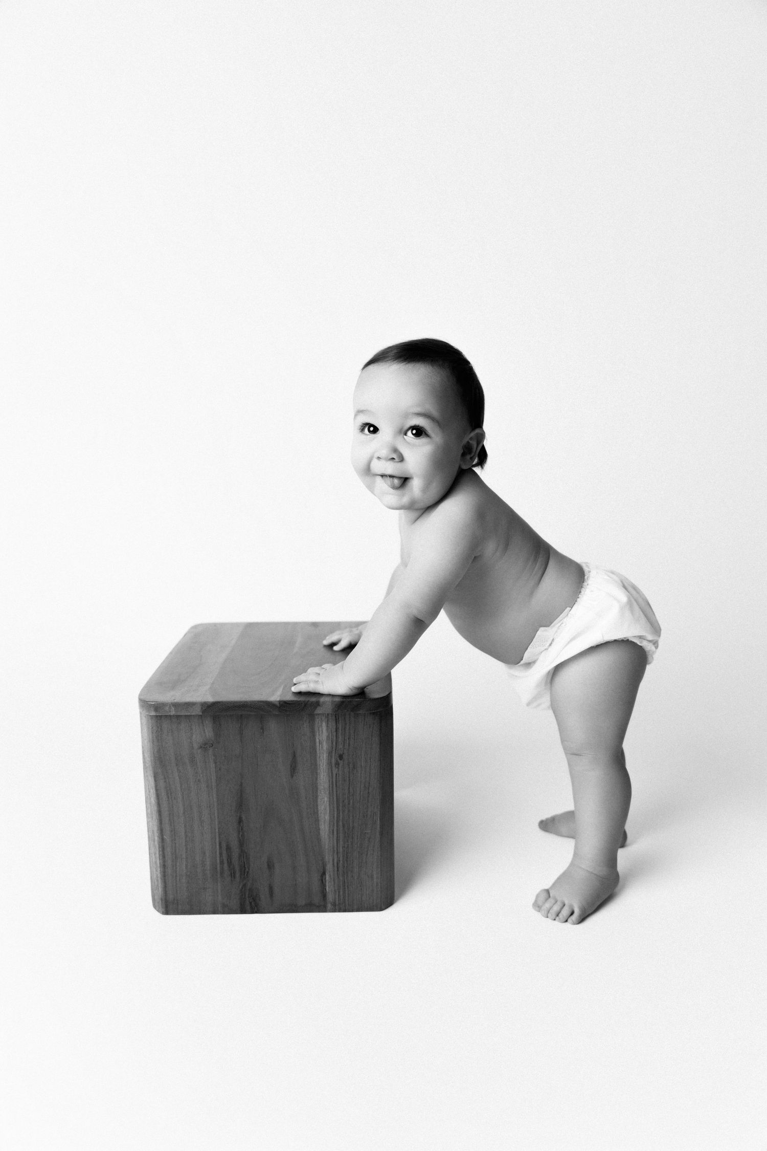 A series of black and white photos showing a baby playfully peeking and interacting with a wooden box.