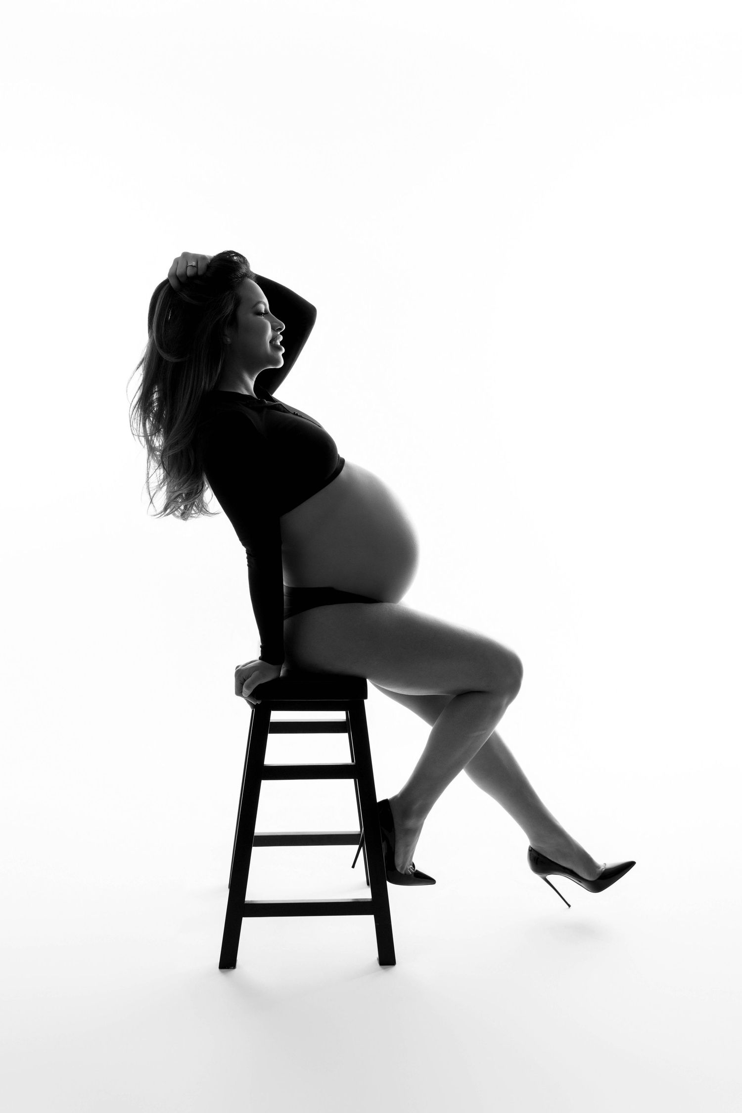 Silhouette maternity portraits with subject posed on chair against white background.