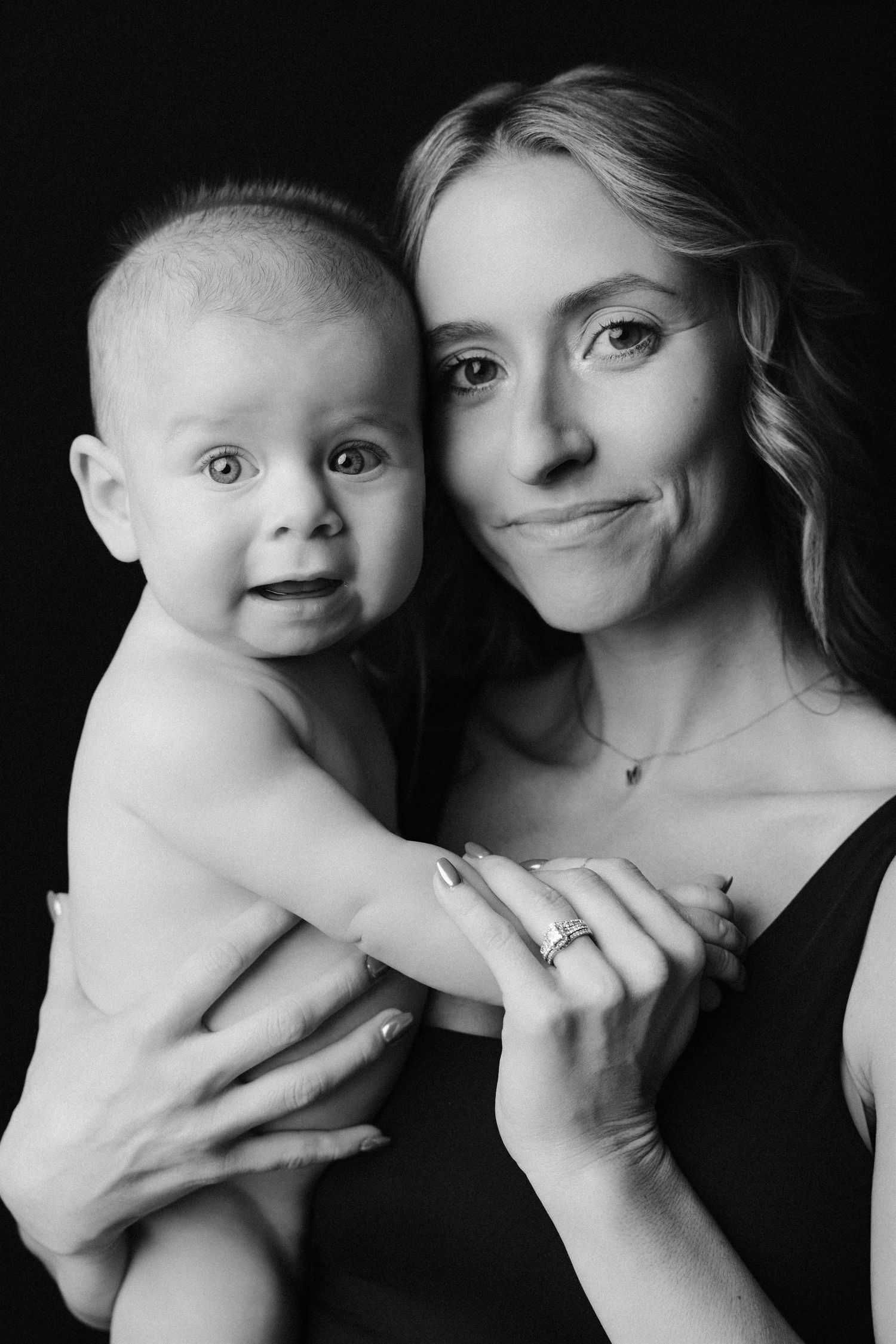 A black and white photo series showing intimate portraits of a mother and baby in artistic poses against dark backgrounds.