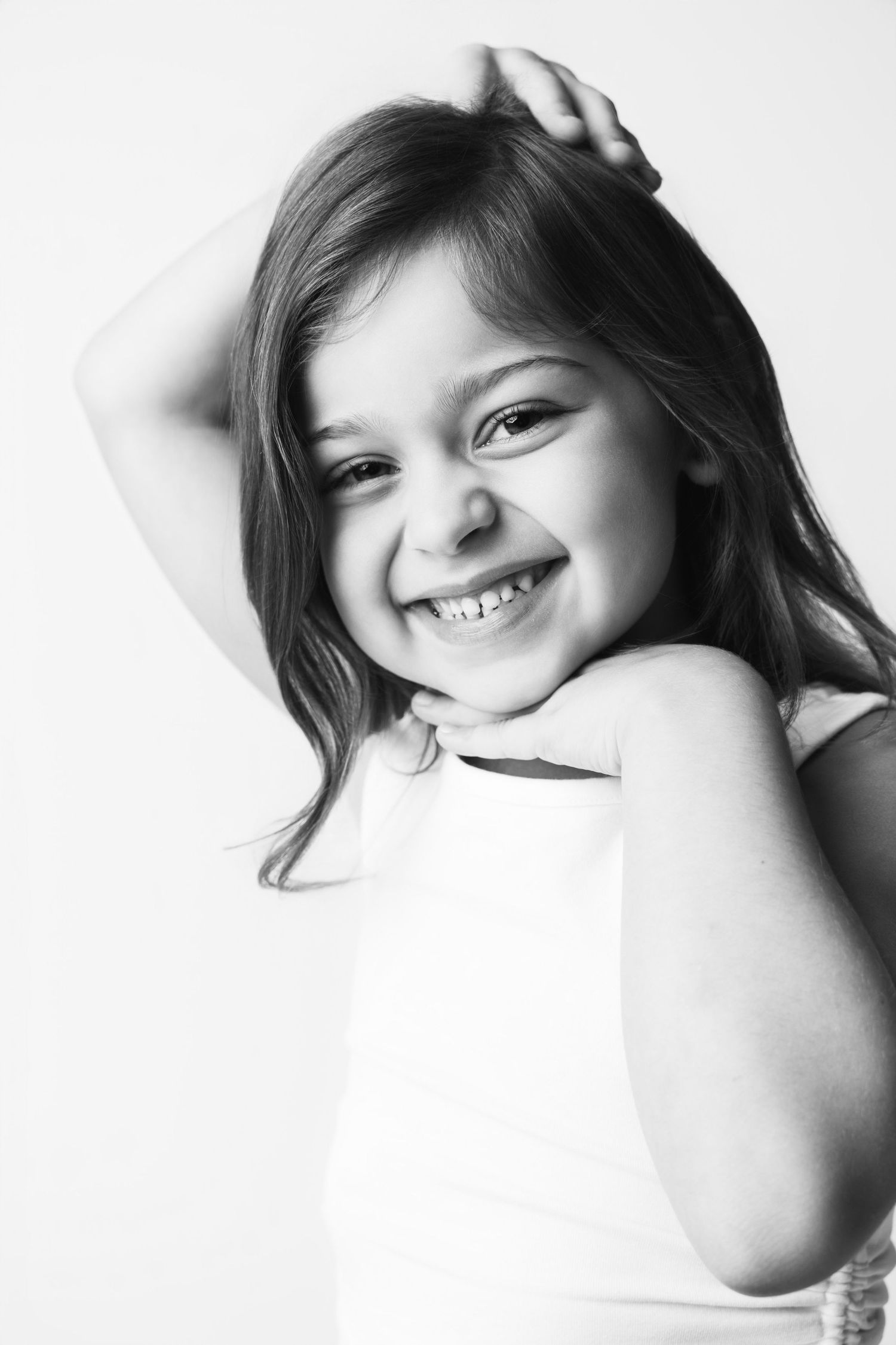 Black and white portrait of a smiling young girl with long hair posing cheerfully against a light background.